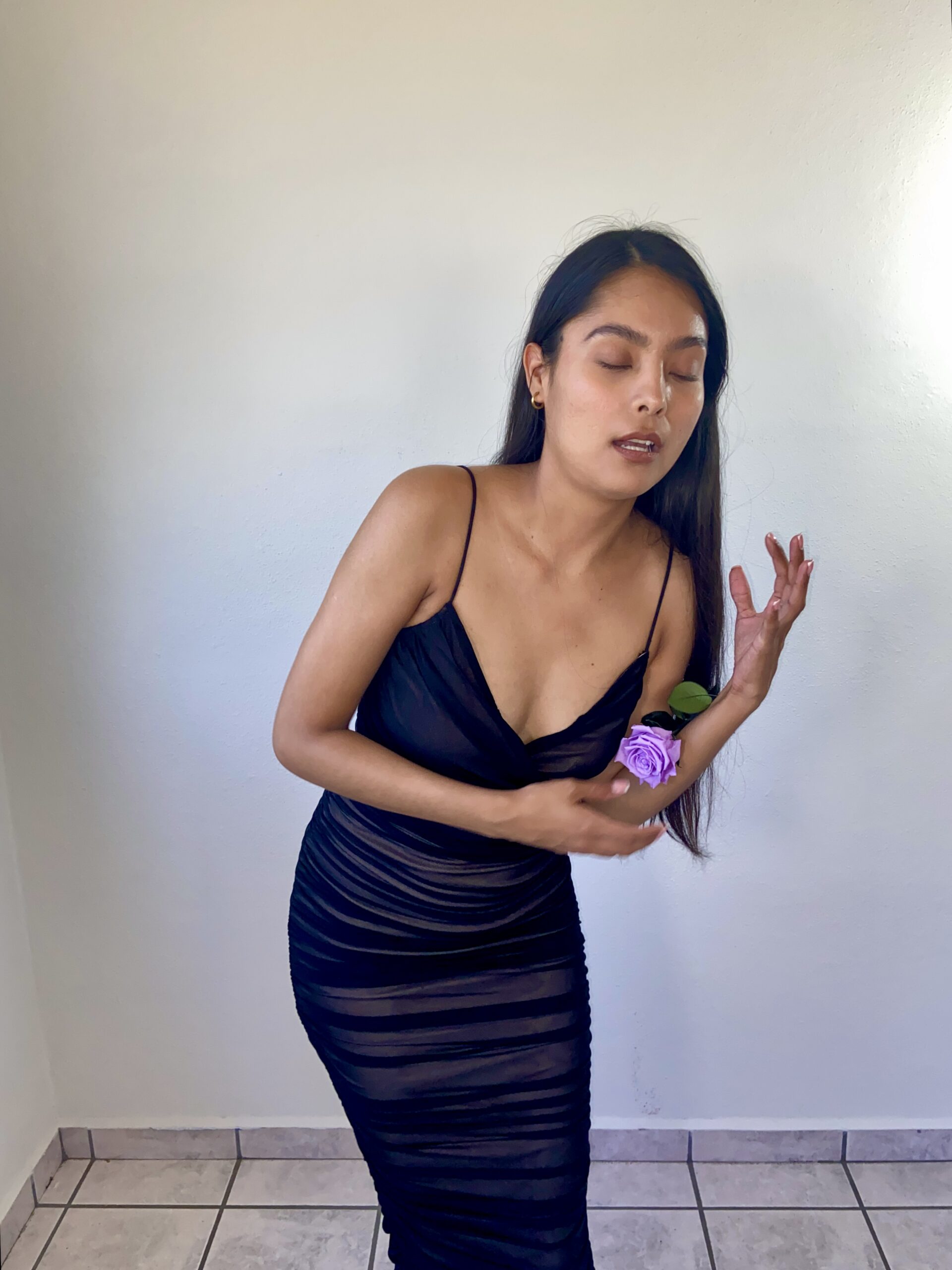 Model Karina Araujo in a black dress and a purple rose in her ear.