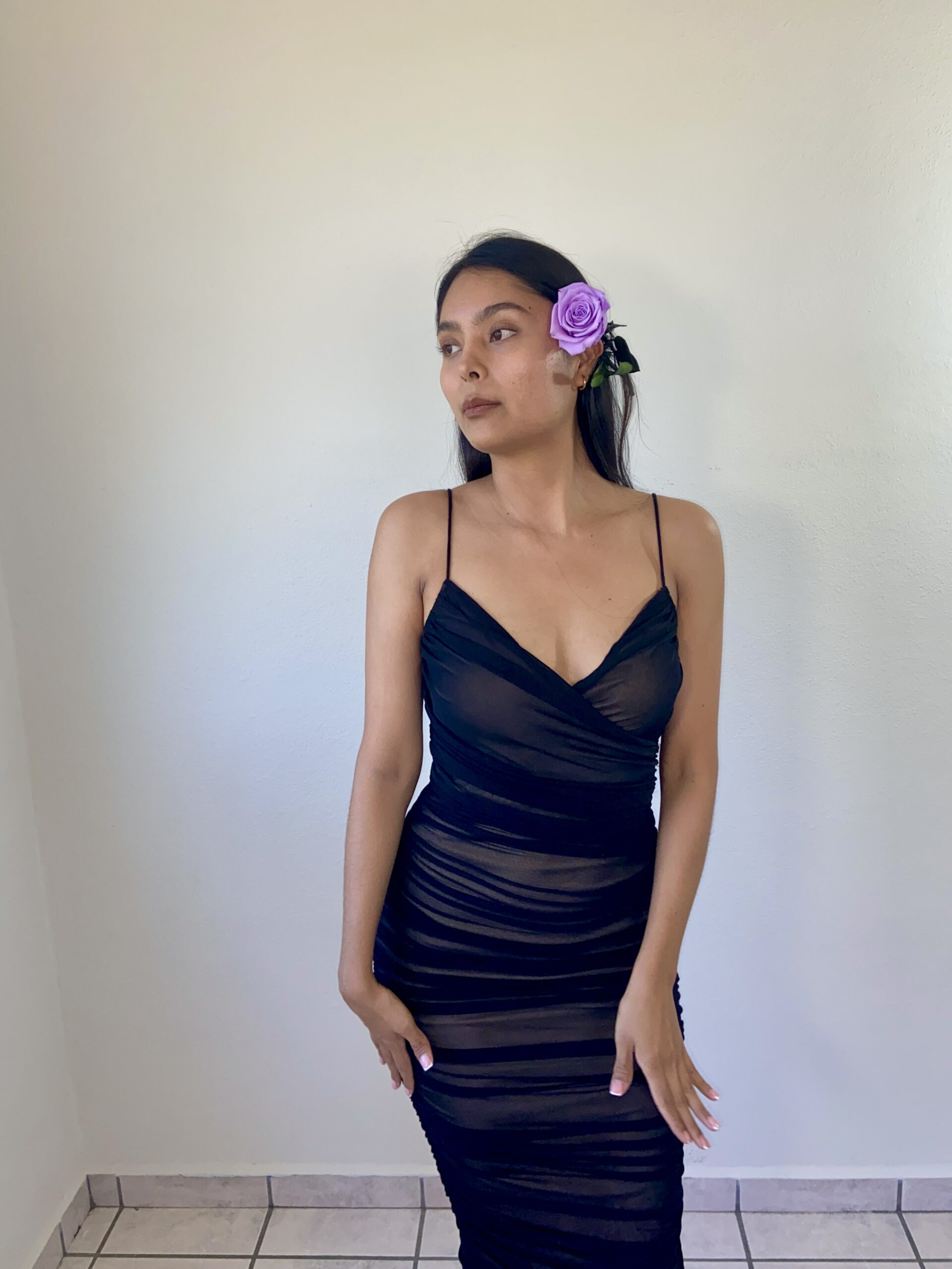 Model Karina Araujo in a black dress and a purple rose in her ear.