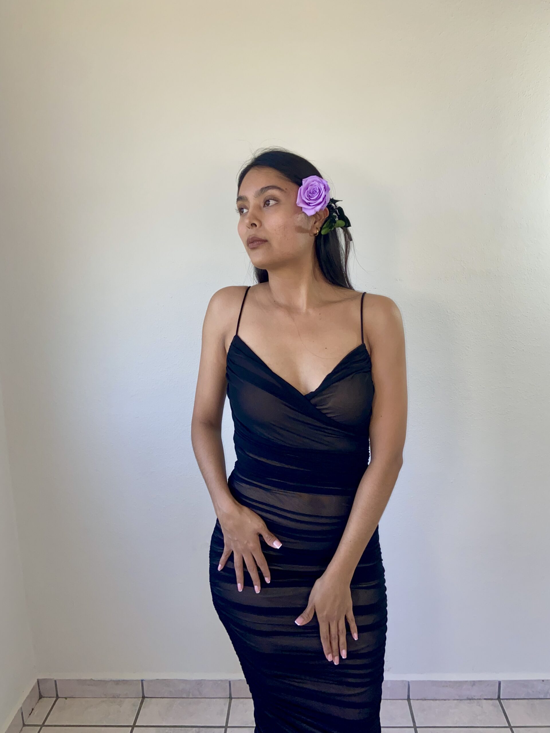 Model Karina Araujo in a black dress and a purple rose in her ear.