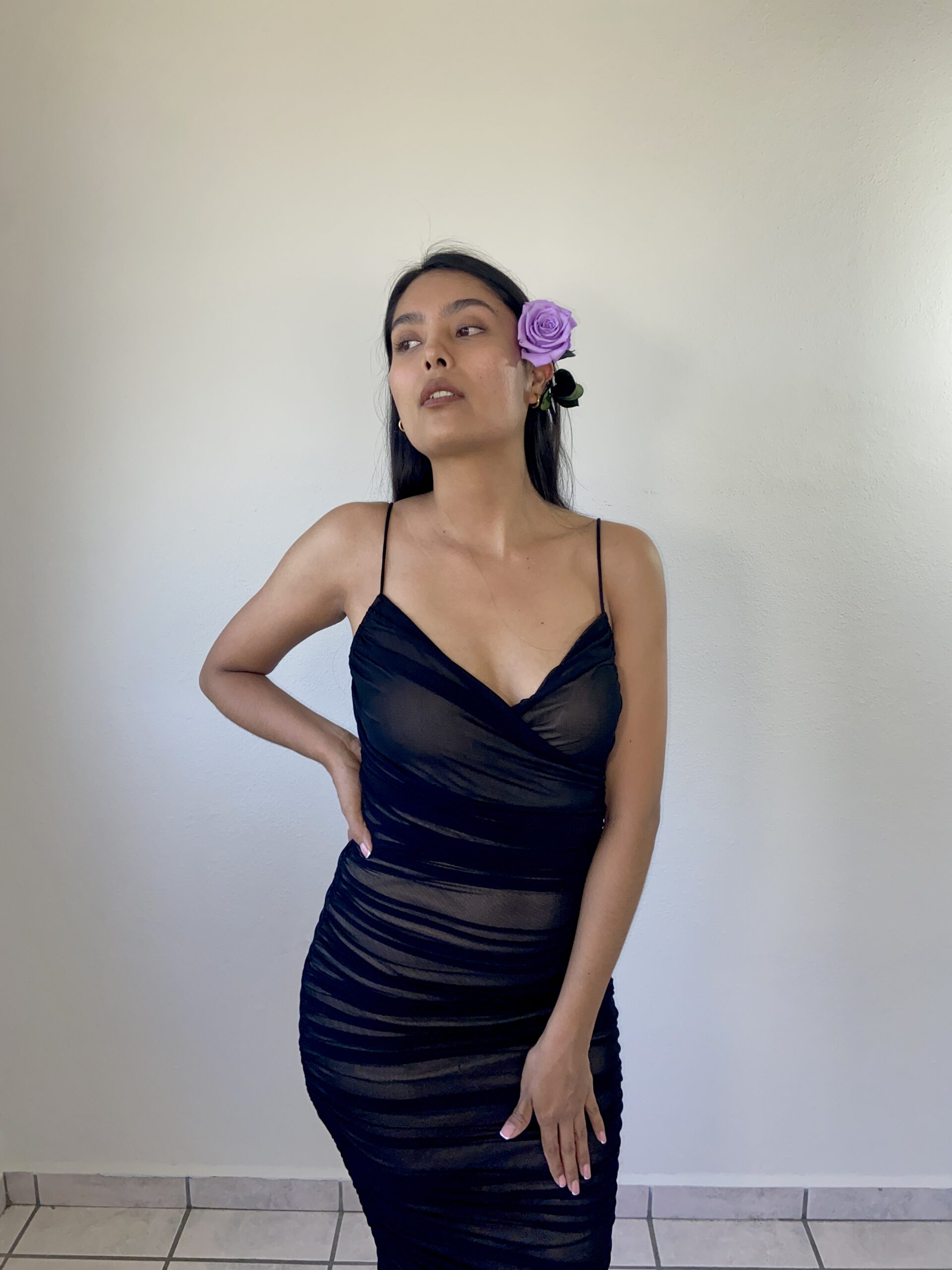Model Karina Araujo in a black dress and a purple rose in her ear.